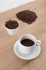 cup of coffee with coffee seeds on wooden table and light brick background