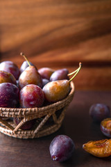 Heap of fresh plums in a wicker basket with wood background.
