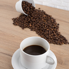 cup of coffee with coffee beans on wooden table and white wall