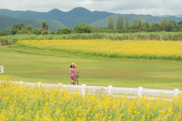 asia woman with a hat in her hand walks in a field with field flowers and smiles sincerely, happy...