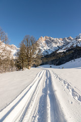 Sunny winter landscape in the nature: Mountain range, footpath, snowy trees, sunshine and blue sky