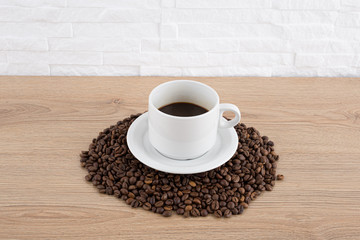 cup of coffee with coffee beans on wooden table and white wall