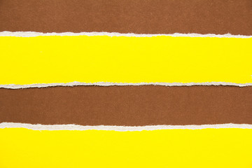 Brown sheet of cardboard with yellow torn horizontal paper stripes. Can be used for text.