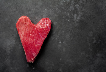 Obraz na płótnie Canvas heart shaped raw beef steak with spices for valentines day on stone background with copy space for your text, concept of cooking dinner for valentines day