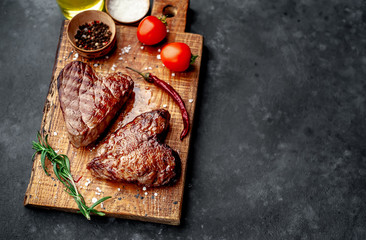 two grilled beef steaks in the form of a heart with spices for Valentine's day on a stone...