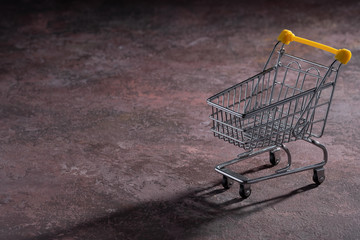 Shopaholic. Buyer. Shopping concept. Close-up. An isolated trolley and shopping basket on a wine brown background bisected.