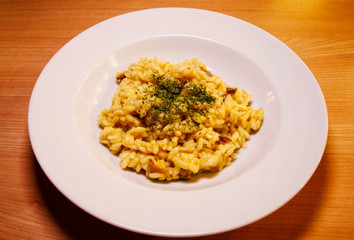 Traditional Italian risotto with mushrooms, saffron, parsley, in a white dish, wooden table