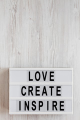 'Love create inspire' words on a lightbox on a white wooden surface, top view. Overhead, from above, flat lay. Copy space.