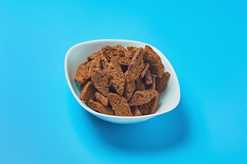 White ceramic bowl full of brown spicy pieces of rusk bread lies on blue desk in sport bar or pub. Close-up