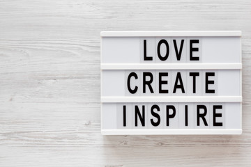 'Love create inspire' words on a modern board on a white wooden surface, top view. Overhead, from above, flat lay. Copy space.