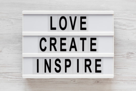 'Love create inspire' words on a lightbox on a white wooden background, top view. Overhead, from above, flat lay.