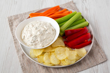Homemade Caramelized Onion Dip with Potato Chips, Celery, Pepper and Carrot on a white wooden surface, low angle view. Close-up.