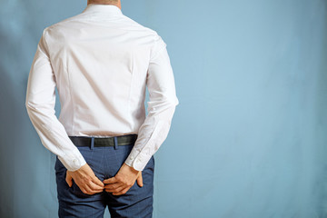 A man in trousers and a white shirt holds on to the back, a symbol of hemorrhoids