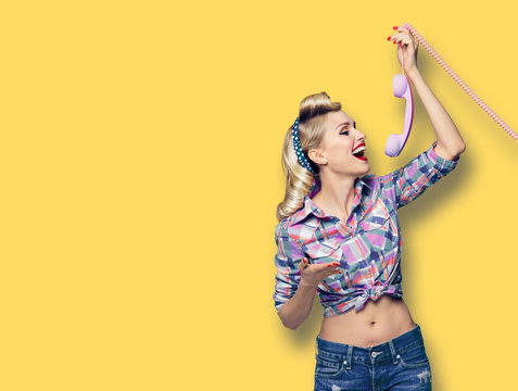 Happy woman holding telephone tube. Excited pin up girl, profile. Blond model at retro fashion and vintage picture. Yellow color background. Copy space for some advertise or text.