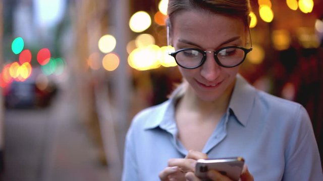 Happy hipster tourist in classic spectacles for vision correction searching information about next famous historic showplace while waiting auto bus on city station, woman typing text message for send