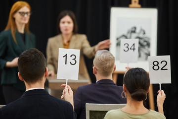 Rear view of people are going to buy modern art while sitting at auction
