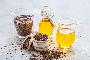 Flaxseed oil in a bottle and ceramic bowl with brown flax seeds and wooden spoon on a white background.