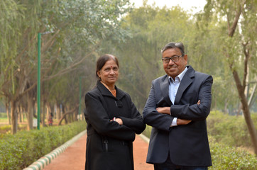 Portrait of a happy looking retired senior Indian man and woman couple smiling and posing with hands crossed / folded in a park outdoor during spring/summer season in Delhi, India. Concept love