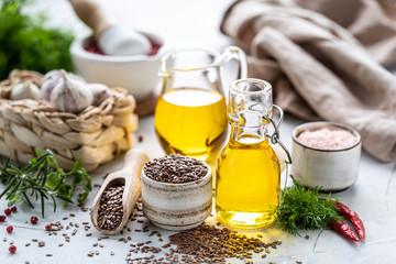 Flaxseed oil in a bottle and ceramic bowl with brown flax seeds and wooden spoon on a white...