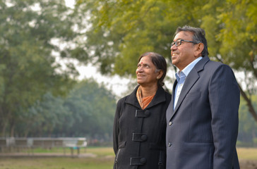 Lifestyle portrait shot of a happy looking senior retired Indian couple in park/outdoor. The wife talks to her husband while looking at  a distance during winters in New Delhi, India