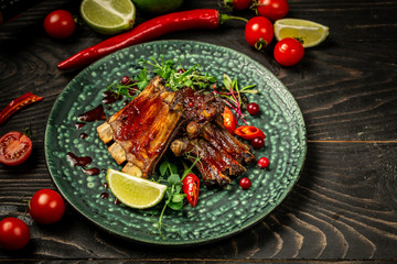 Roasted sliced barbecue pork ribs on a modern plate with berry sauce and cherry tomatoes, lime and chilli. pea sprouts, sunflower and beet. Top view