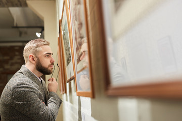 Serious bearded man examining the detail of painting while visiting the art gallery