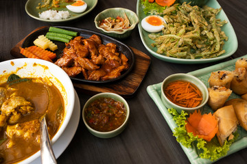 Thai food on wooden tableware, fish curry, grilled pork with sauce, salad, fried vegetables, spring rolls