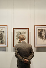 Rear view of man in formal wear standing and looking at paintings on the wall at art gallery