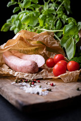 Ring of traditional country homemade sausage in a composition with spices, herbs, tomatoes and wooden cutting board.