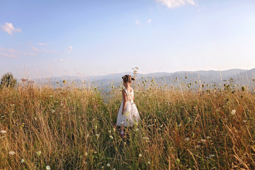 Fototapeta na wymiar Cute girl dancing through a beautiful meadow with wheat and flowers in the mountains