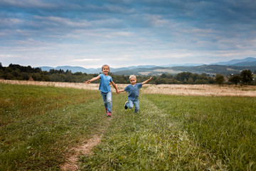 Naklejka na ściany i meble Cute girl with her brother running together in beautiful meadow in the mountains