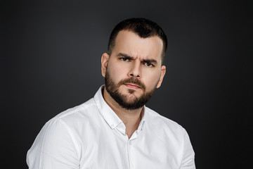 man gazes steadily. Close-up portrait of handsome bearded man in white shirt looking at camera isolated on black background