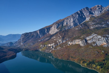 Naklejka na ściany i meble Aerial view of Lake Molveno, north of Italy. In the background rocky alps, blue sky. Reflection of mountains in water. Autumn season. Multi-colored palette of colors