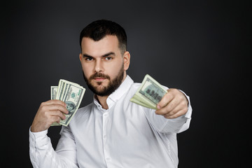 bearded man holding money banknotes and looking at the camera isolated on black background. man gives money