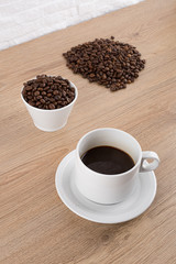 cup of coffee with coffee seeds on wooden table and light brick background