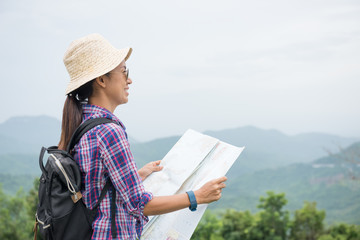 Young woman Traveler and adventure with backpack and hat relaxing outdoor with rocky mountains on background, looking a map. Summer vacations and Lifestyle hiking concept.