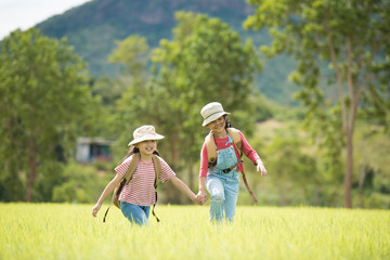 Two little girl carrying a backpack and wearing a hat. Running around in the grassland Children walk and enjoy the surrounding nature. She enjoys traveling in the summer.
