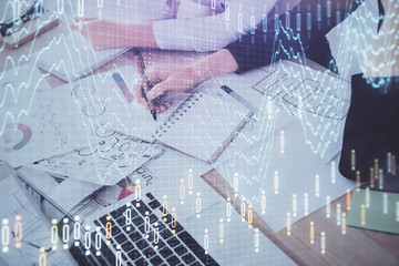 A woman hands writing information about stock market in notepad. Forex chart holograms in front. Concept of research. Double exposure