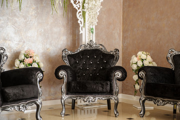 close up photo of a luxury interior: a vintage black armchairs and sofa with silver details near a  wedding round arch decorated with flowers