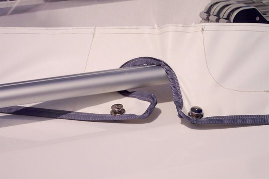 The details of the passage of a tube inside the cockpit protection of a sailsboat. This PVC part close-up with window low section. It s a sprayhood. Details close-up