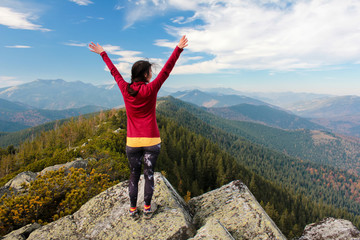 The young girl  at the top of the mountain raised her hands up on blue sky background. The woman climbed to the top and enjoyed her success.  Back view
