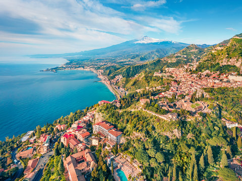 View from flying drone. Sunny morning view of Taormina town and Etna volcano on background. Nice spring seascape of Mediterranean sea. Splendid view of Sicily, Itale, Europe.