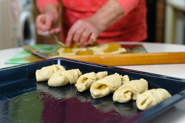 An old woman (80 years old) cooks at home in the kitchen, makes homemade cookies. Close-up, sharpness on a baking sheet with cookies.