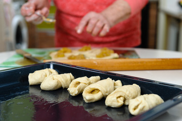 An old woman (80 years old) cooks at home in the kitchen, makes homemade cookies. Close-up, sharpness on a baking sheet with cookies.