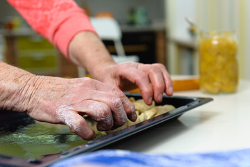 An old woman (80 years old) cooks at home in the kitchen, makes homemade cookies. Puts cookies on a baking sheet. Close-up.