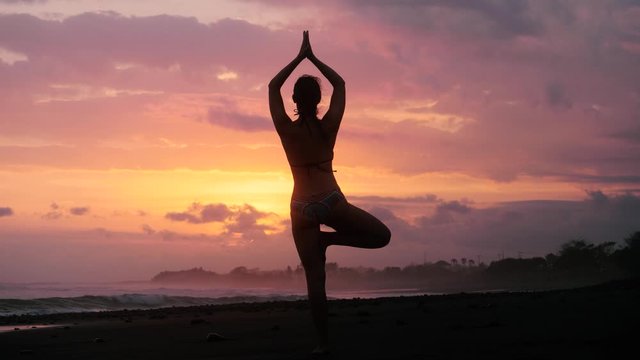 SLOW MOTION Young woman yoga pose practice at sunset on a tropical beach in bikini