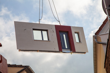 Fertighaus Bauteil mit Haustür am Kran beim Einschweben zur Montage zwischen Häusern