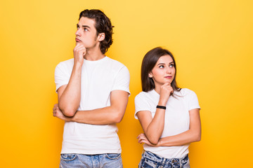 Image of happy young people man and woman in basic clothing thinking and touching chin while looking aside over yellow background