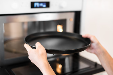 Girl puts a black baking dish in the oven in the kitchen