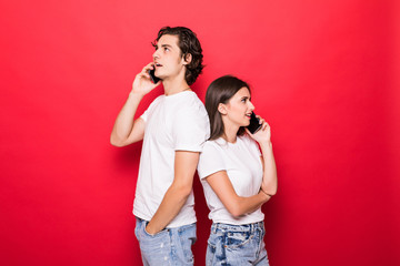 Attractive young couple talking on their smartphones isolated on red background